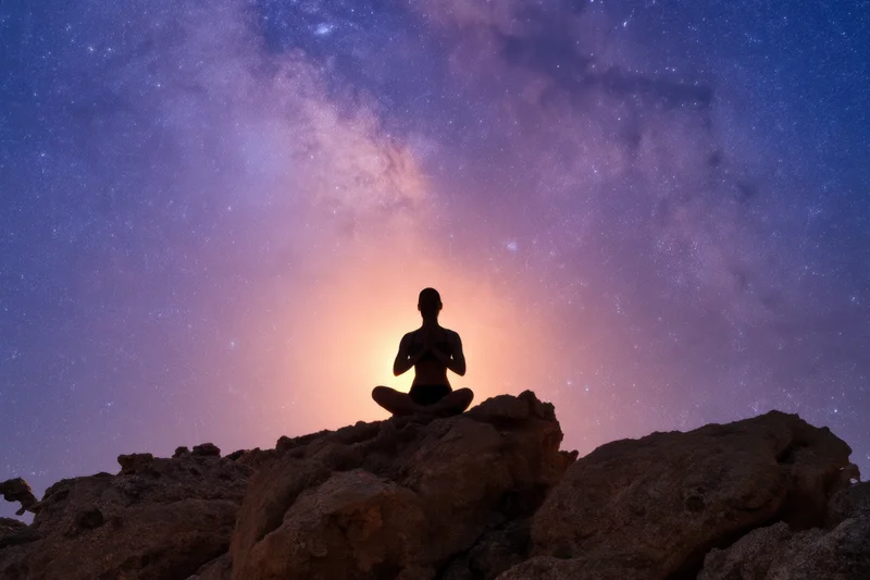 Woman meditating in lotus pose on rocky outcrop under starry night sky