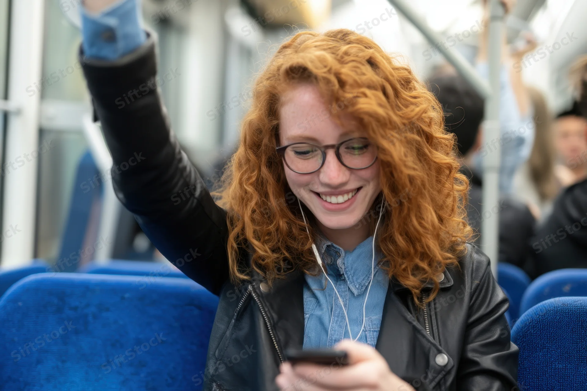 Young woman with curly red hair and glasses smiling while using smartphone on a bus