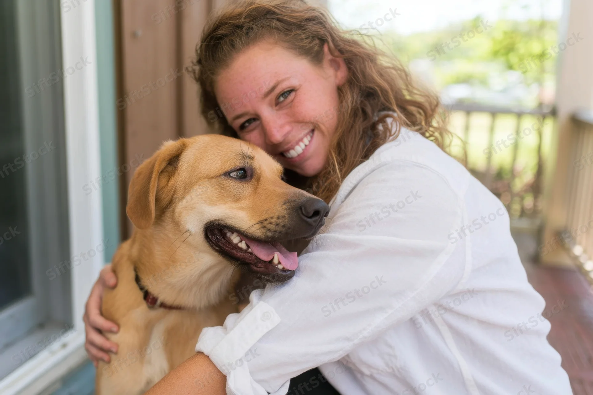 Woman hugging a tan dog on a porch outdoors