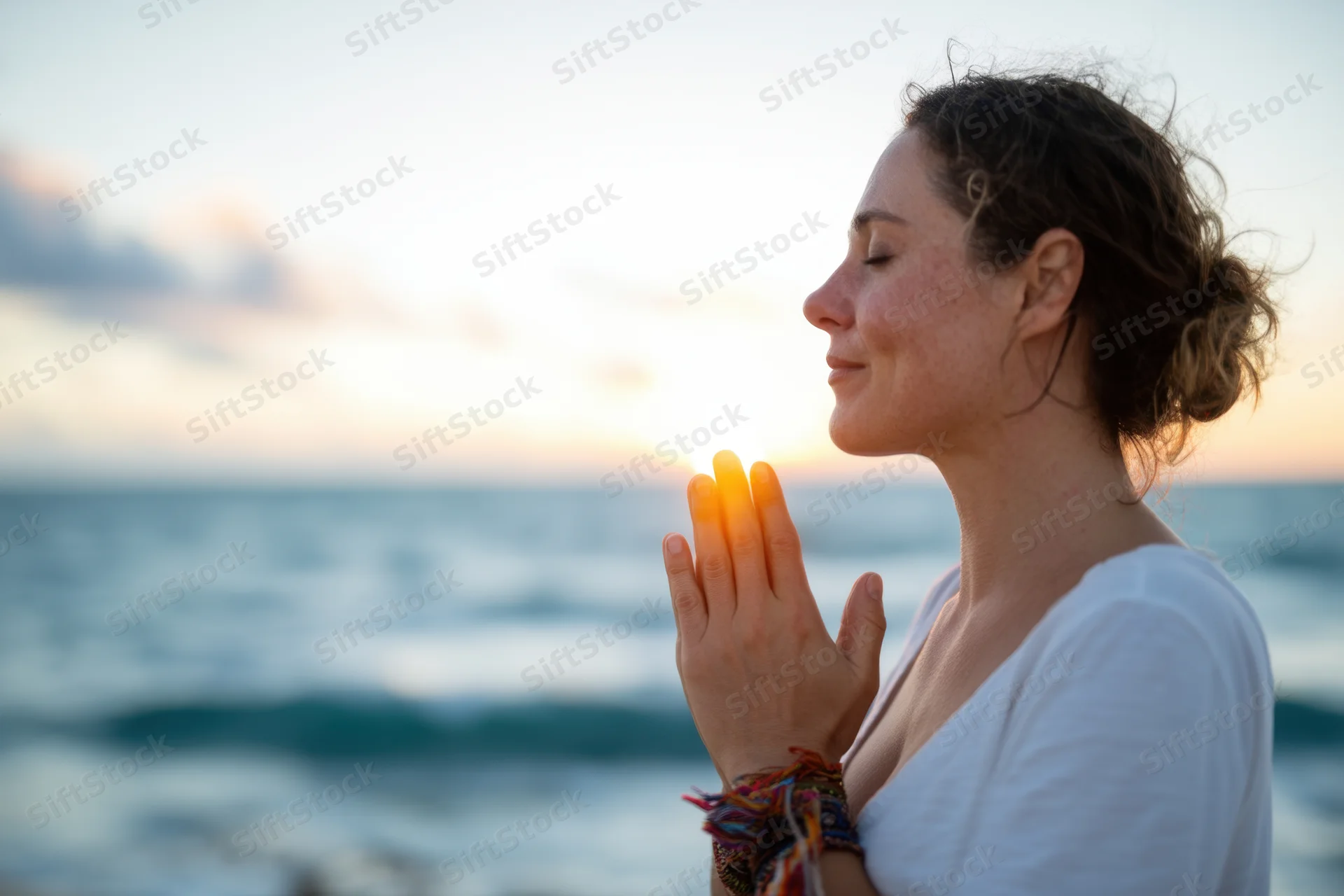 Woman in profile with hands pressed together in prayer by the ocean at sunset