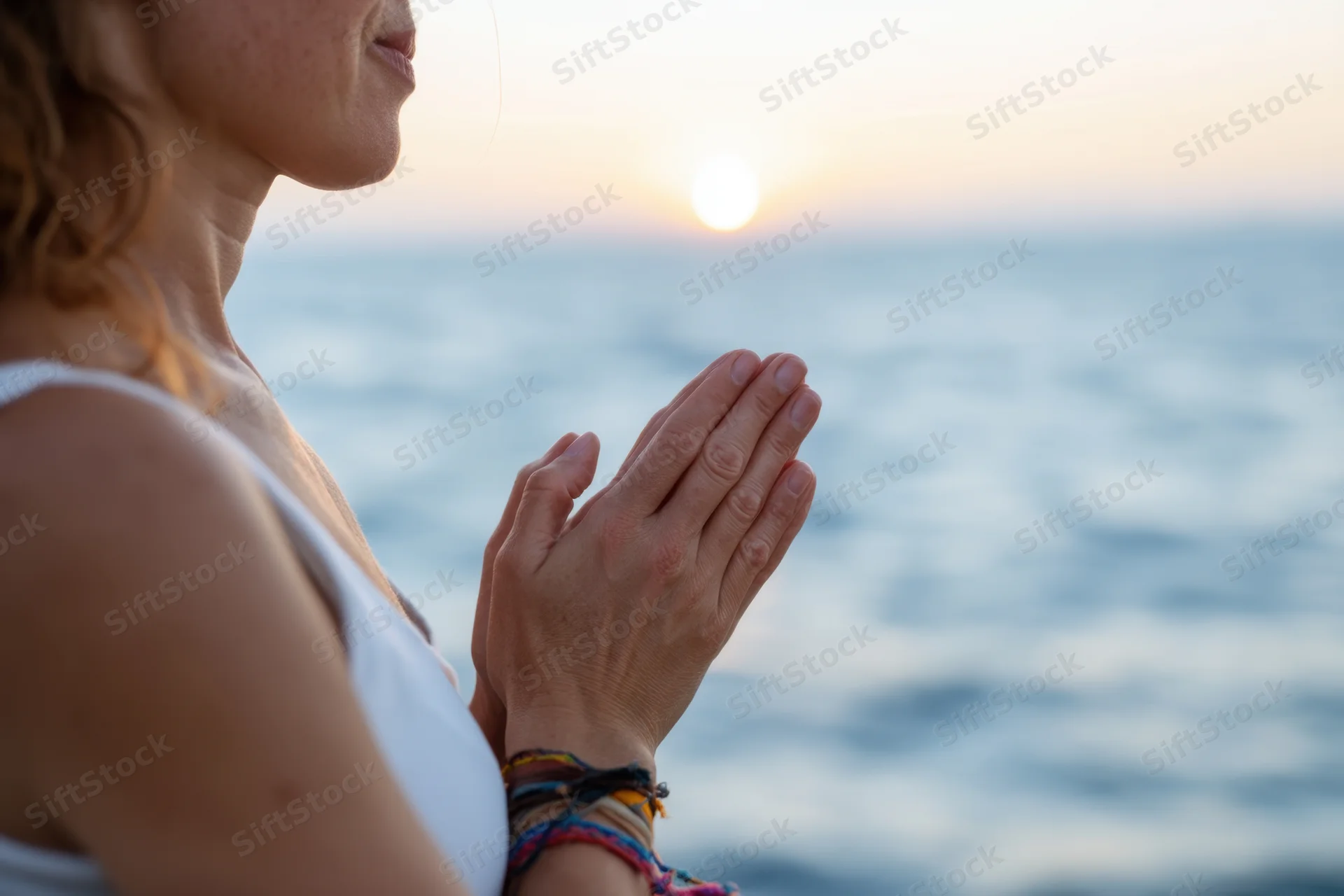 Woman in profile with hands pressed together in prayer by the ocean at sunset