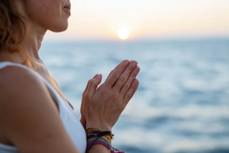 Woman in profile with hands pressed together in prayer by the ocean at sunset