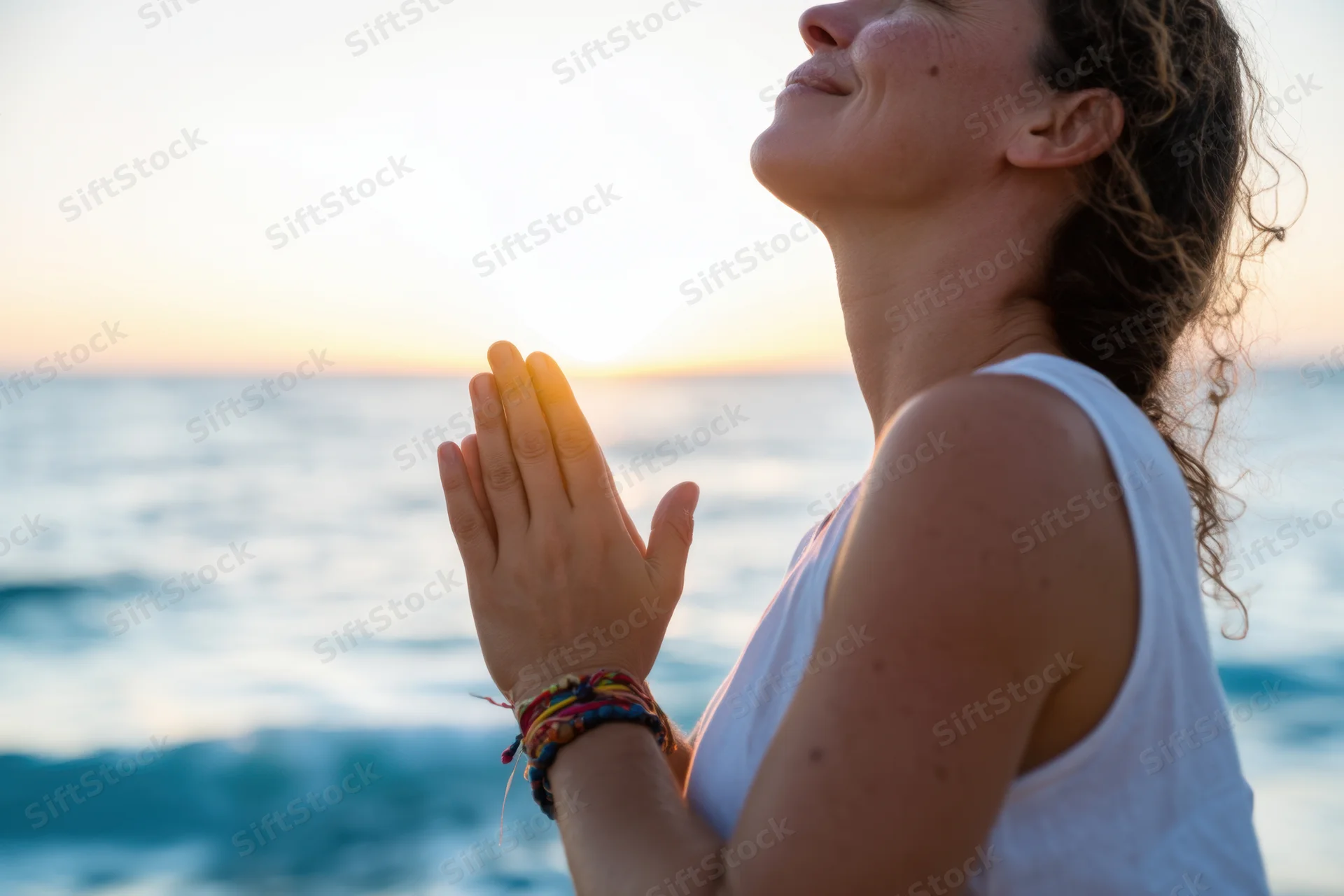 Woman in profile with hands pressed together in prayer by the ocean at sunset