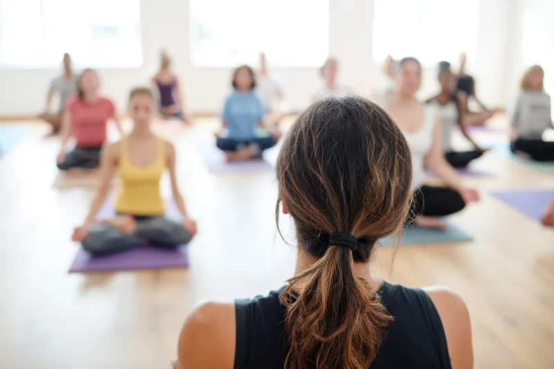 Woman instructor leading yoga class in studio with group seated on mats facing her