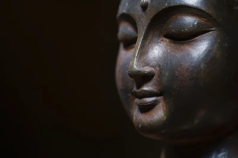 Close-up profile of a serene buddha statue head with closed eyes in shadowed lighting