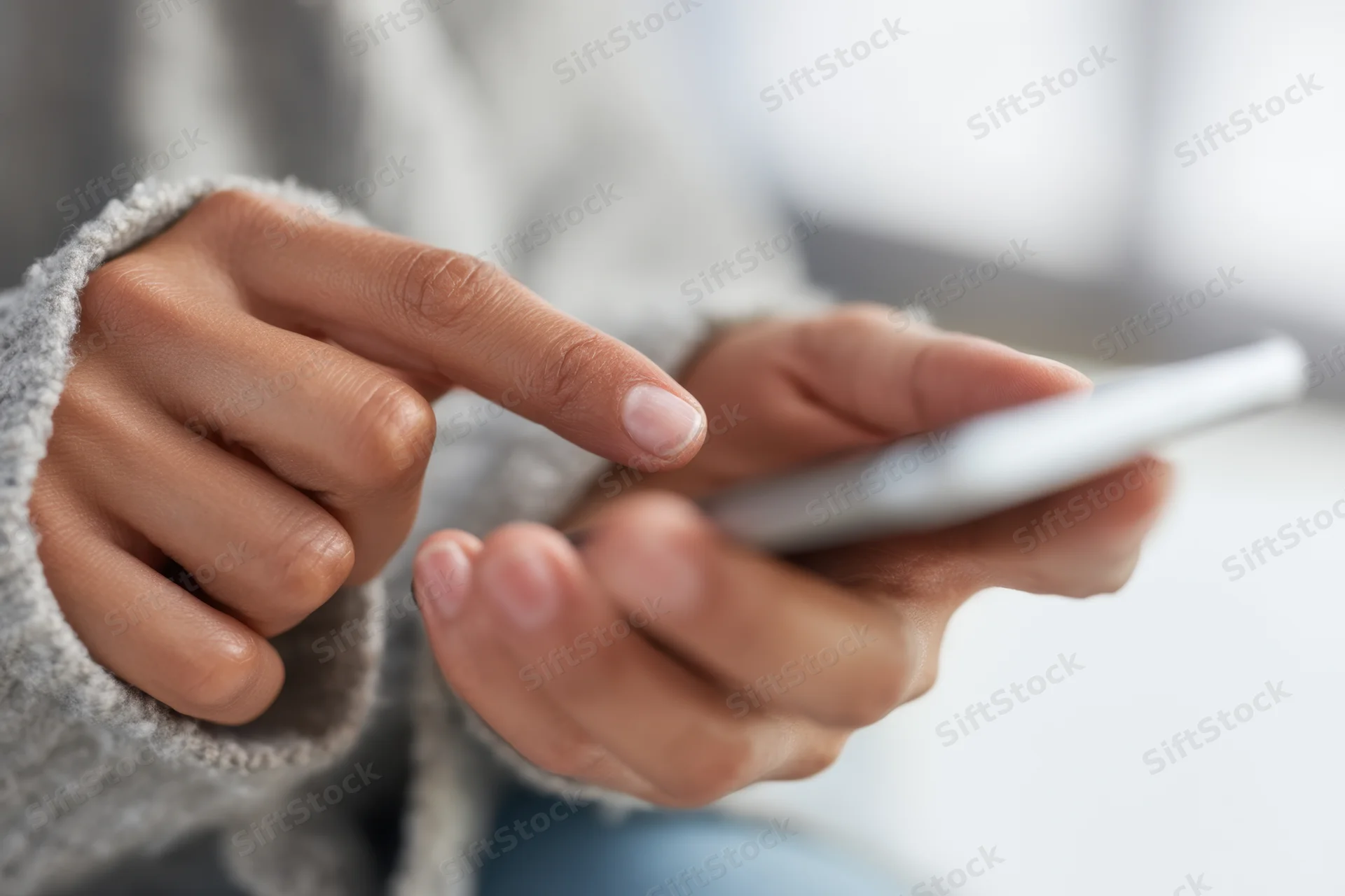 Close-up of hands tapping a smartphone while wearing a gray sweater indoors