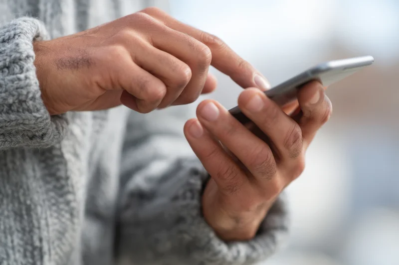 Hands tapping a smartphone while wearing a gray knitted sweater