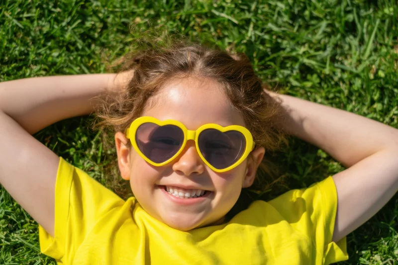 Smiling girl wearing yellow heart-shaped sunglasses lying on green grass