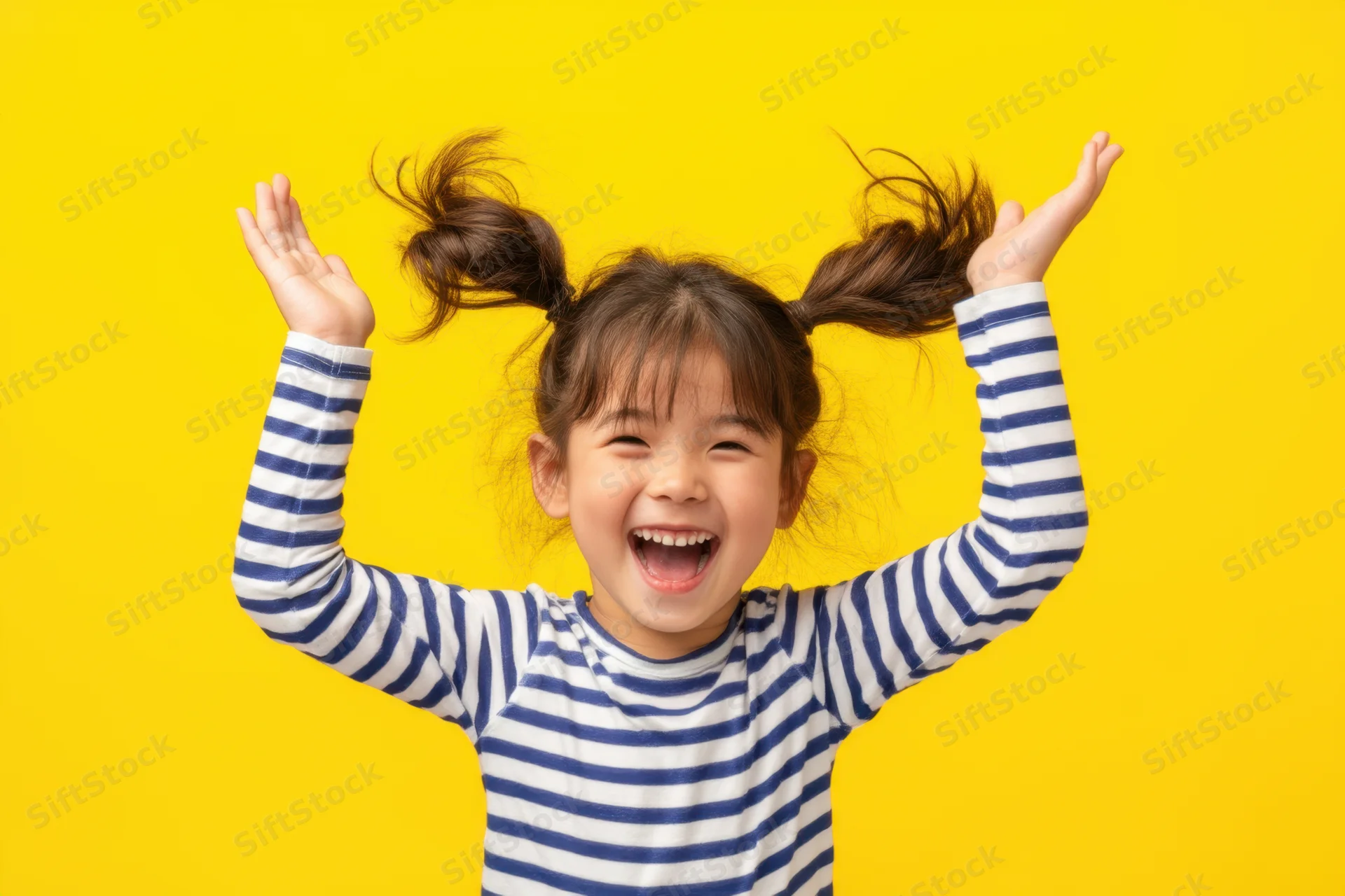 Young girl with pigtails laughing joyfully with arms raised against yellow background