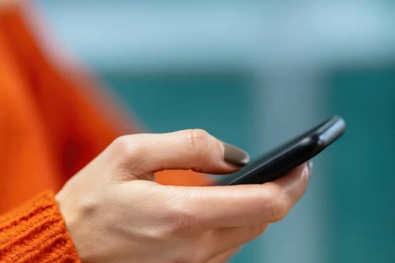 Hand holding a black smartphone with orange sweater sleeve visible