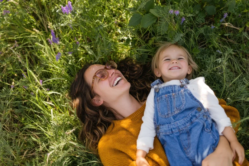 Mother and child laughing while lying on grass in a sunlit meadow