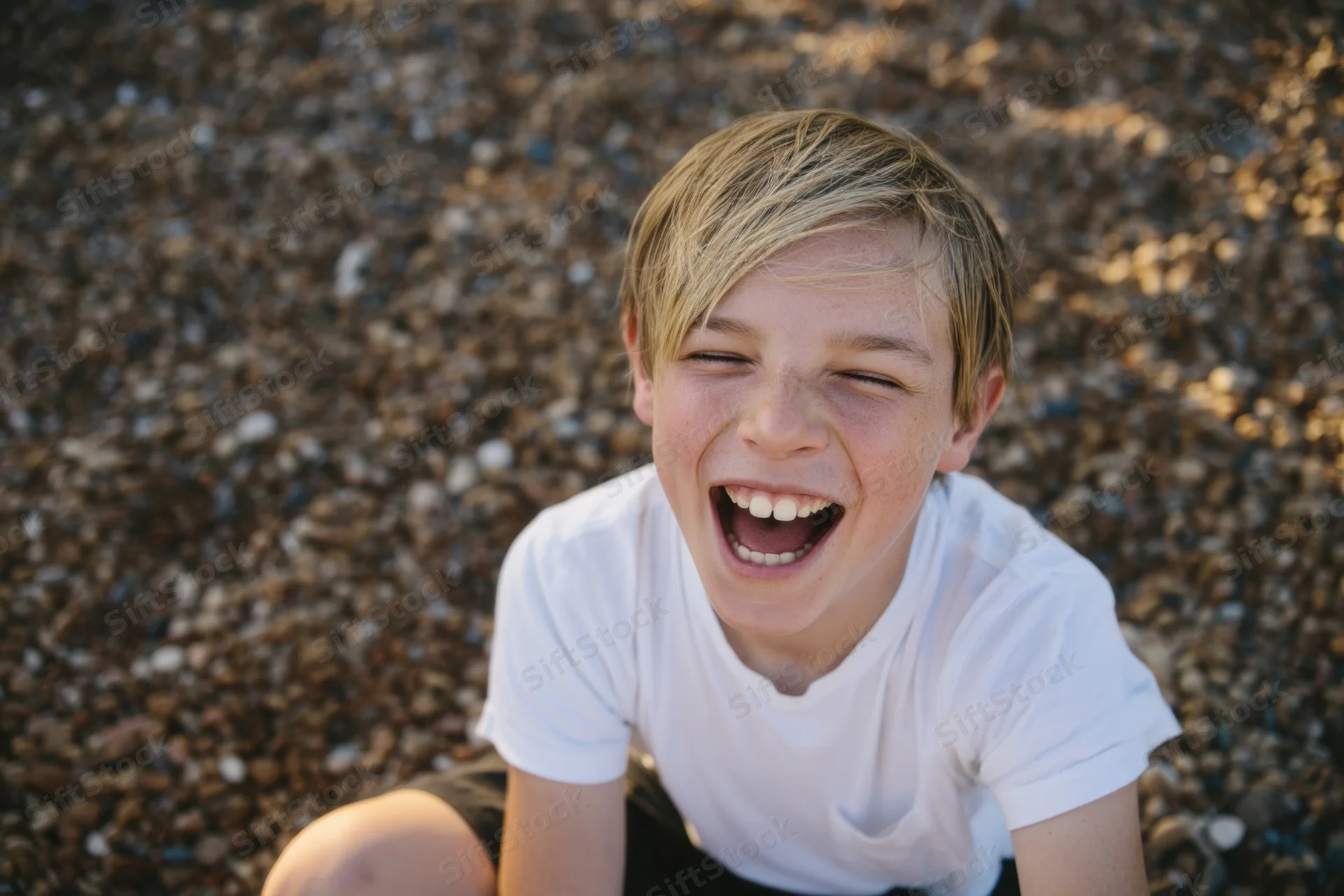 Young boy laughing joyfully on a pebble beach in sunlight