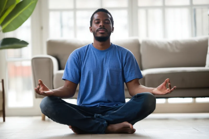 Man meditating cross-legged on floor in bright living room