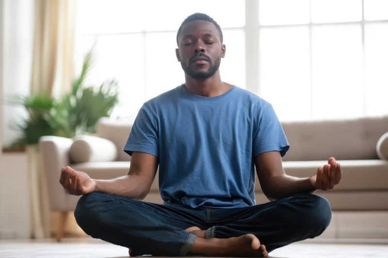 Man meditating cross-legged on floor in bright living room