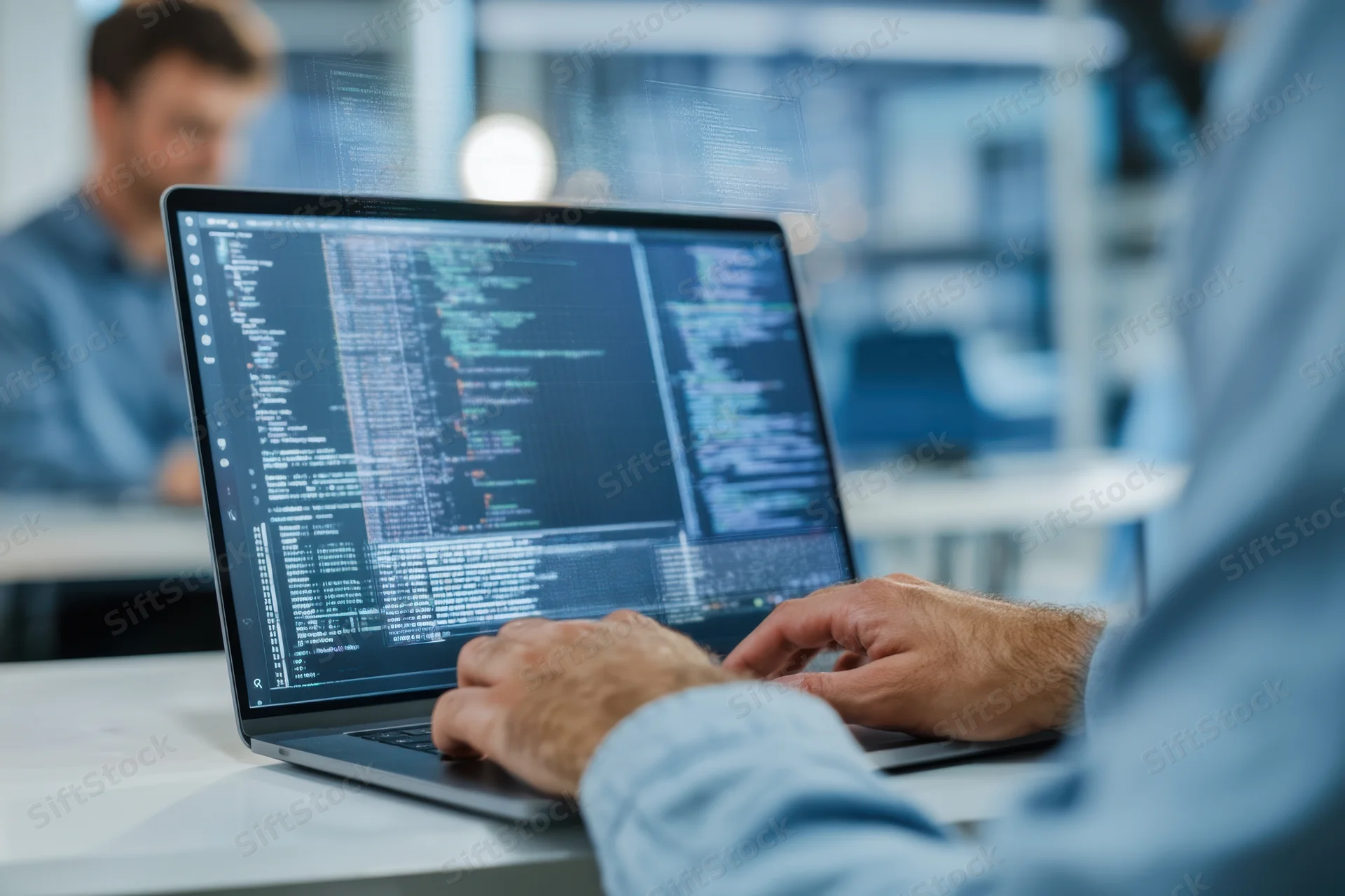 Programmer typing code on laptop in office workspace with holographic display overlay