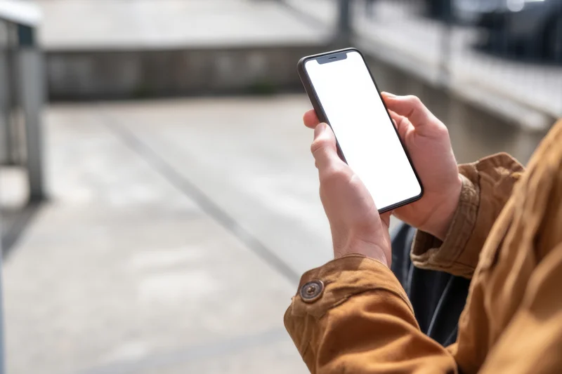 Person holding smartphone with blank white screen outdoors on city sidewalk