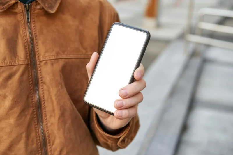 Person holding smartphone with blank white screen outdoors in city street