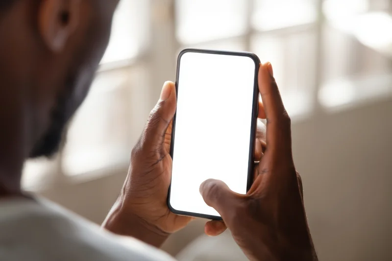 Man holding smartphone with blank white screen over shoulder indoors near window