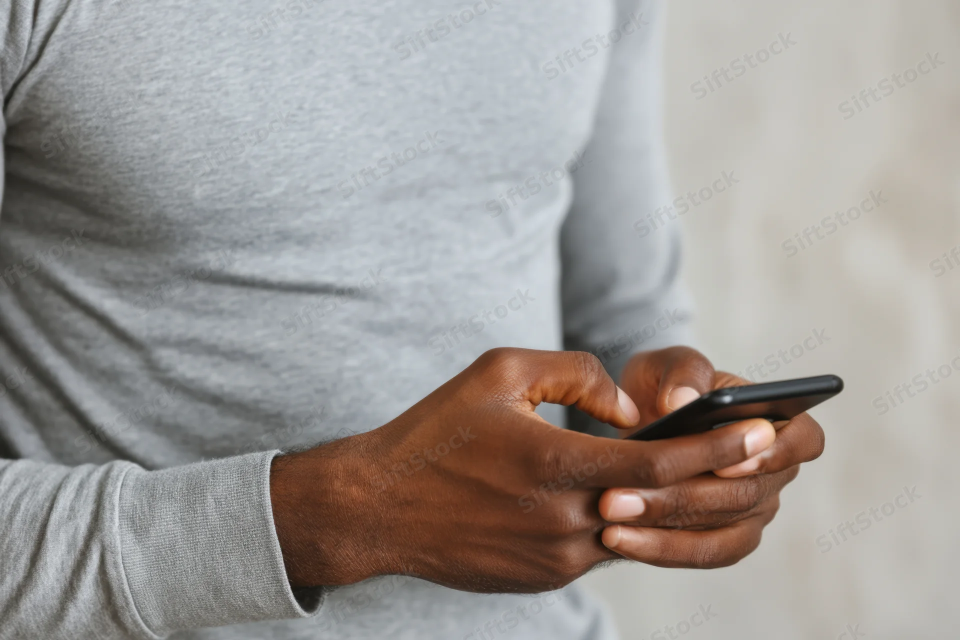Man using smartphone with thumbs typing on touchscreen while wearing gray longsleeve shirt
