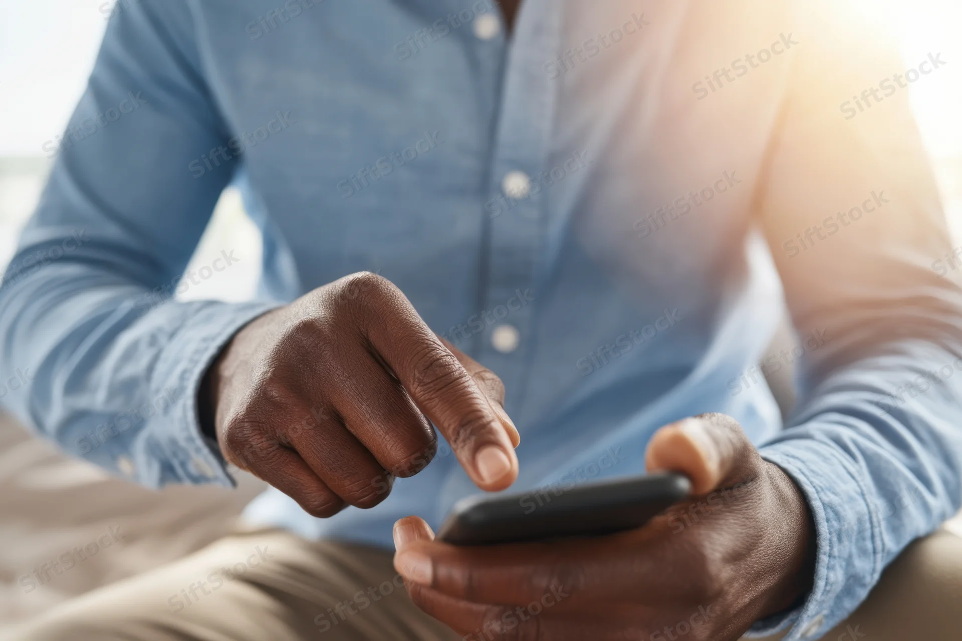 Man tapping smartphone with finger while sitting indoors in light blue shirt