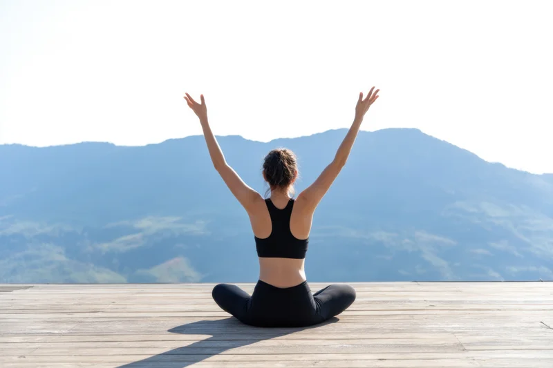 Woman practicing yoga seated cross-legged on wooden deck with mountains in background