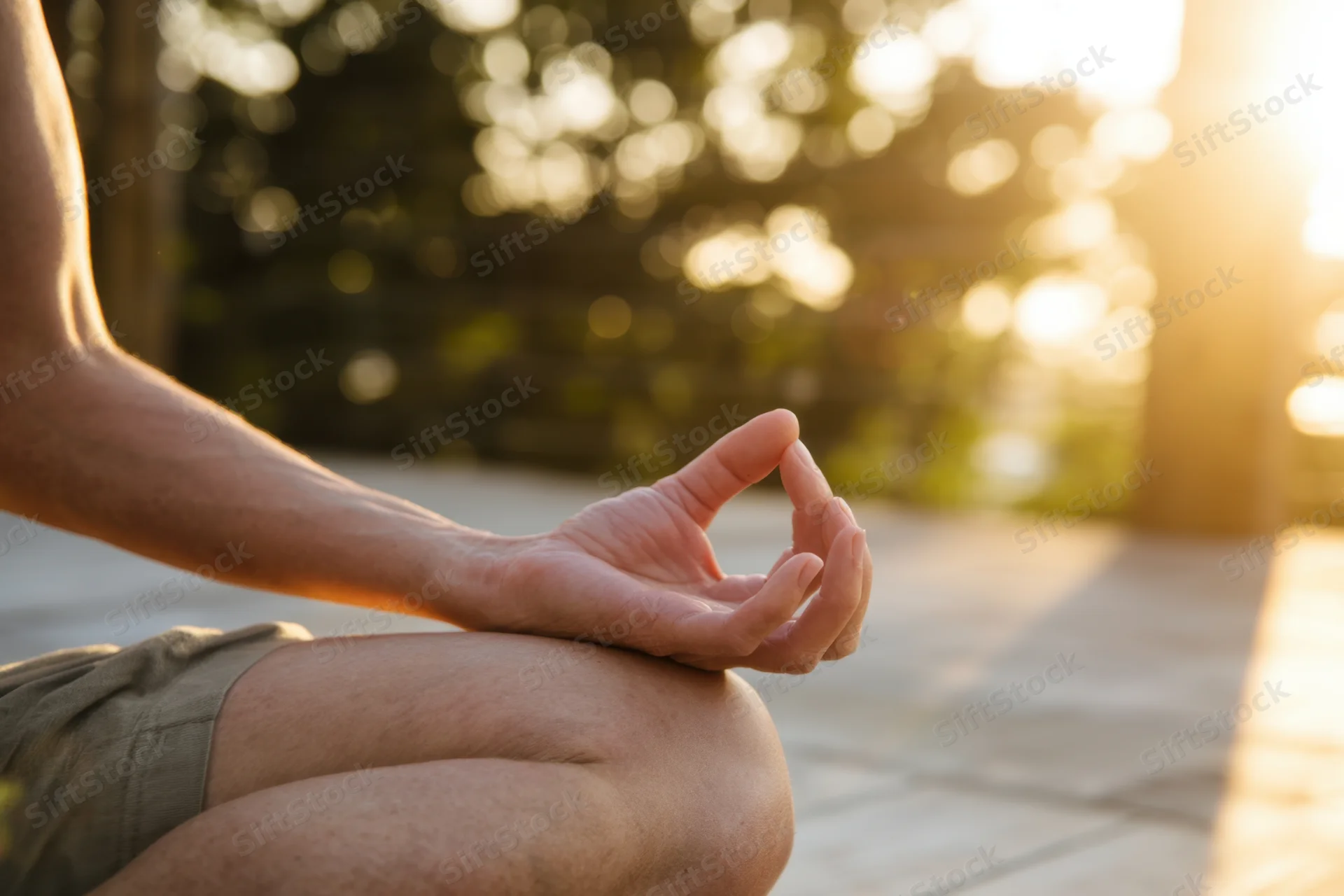 Person sitting cross-legged in meditation with hand in mudra gesture on sunlit wooden deck