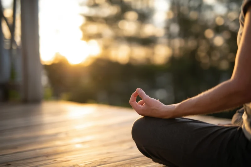 Person sitting cross-legged in meditation pose on wooden deck at sunrise