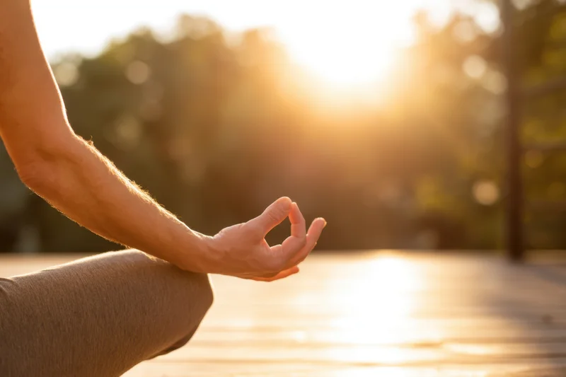 Hand in mudra gesture during yoga practice on wooden deck at sunrise