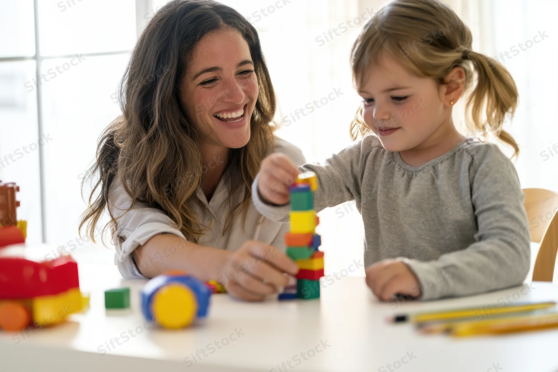Woman and young girl smiling while stacking colorful blocks at a table