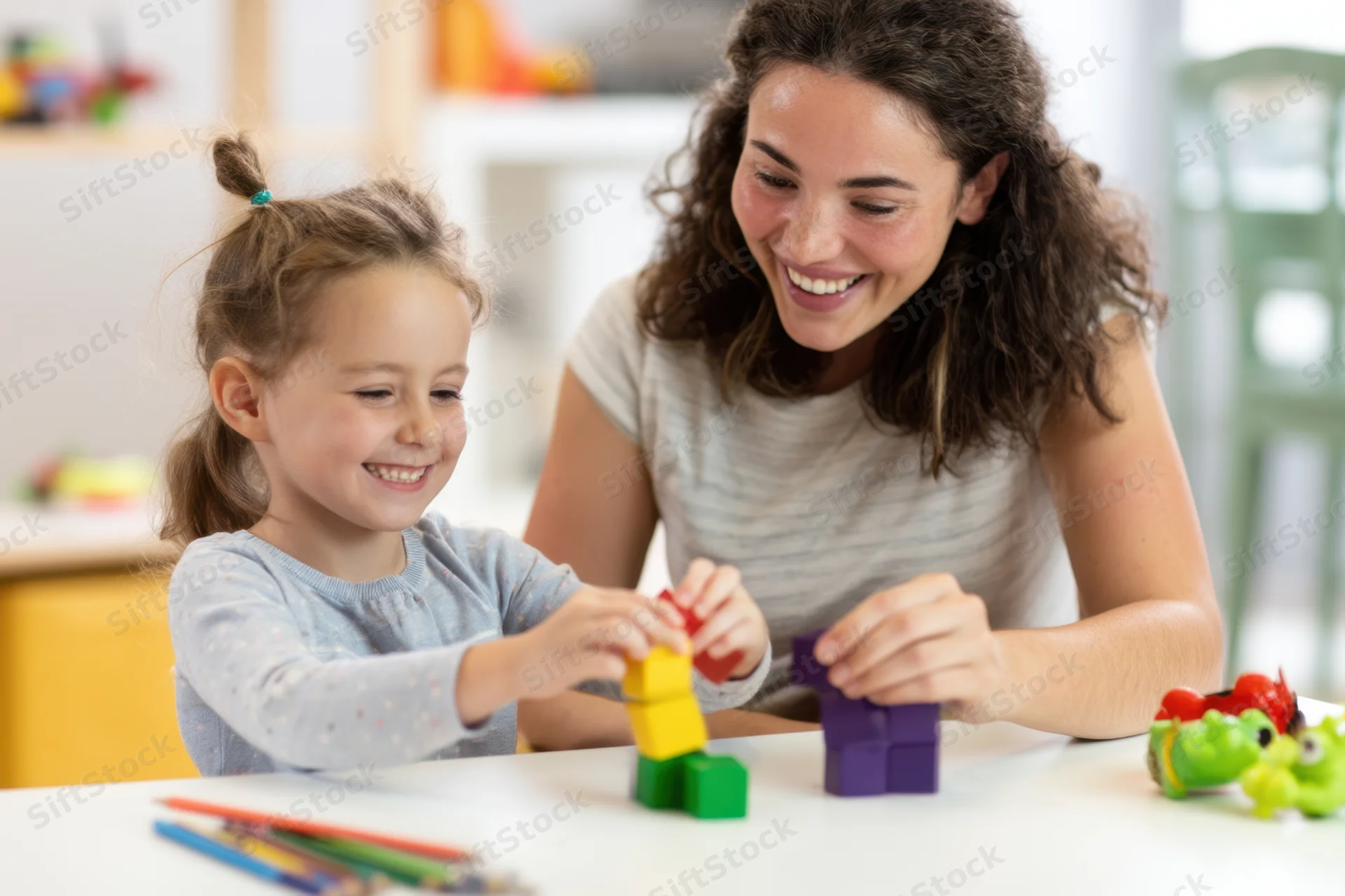 Woman and young girl smiling while stacking colorful blocks at a table in a home setting