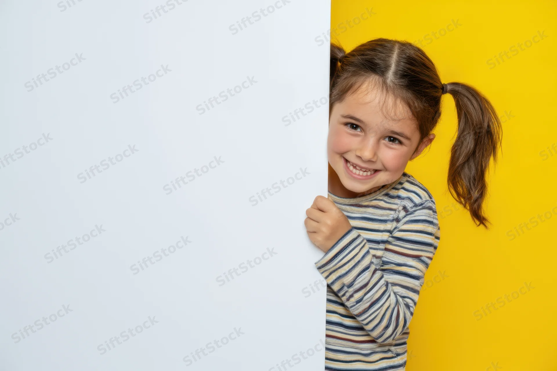 Young girl smiling and peeking from behind a white board against a yellow background