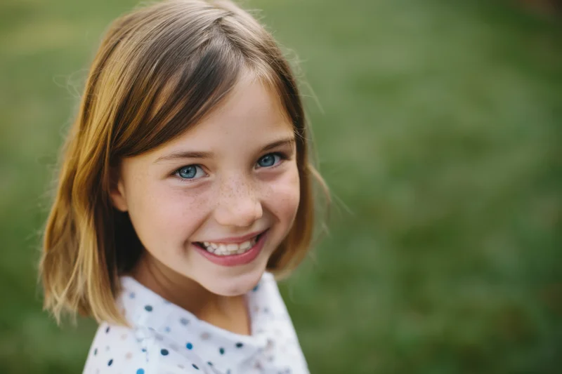 Smiling young girl with shoulder-length light brown hair in a grassy outdoor setting