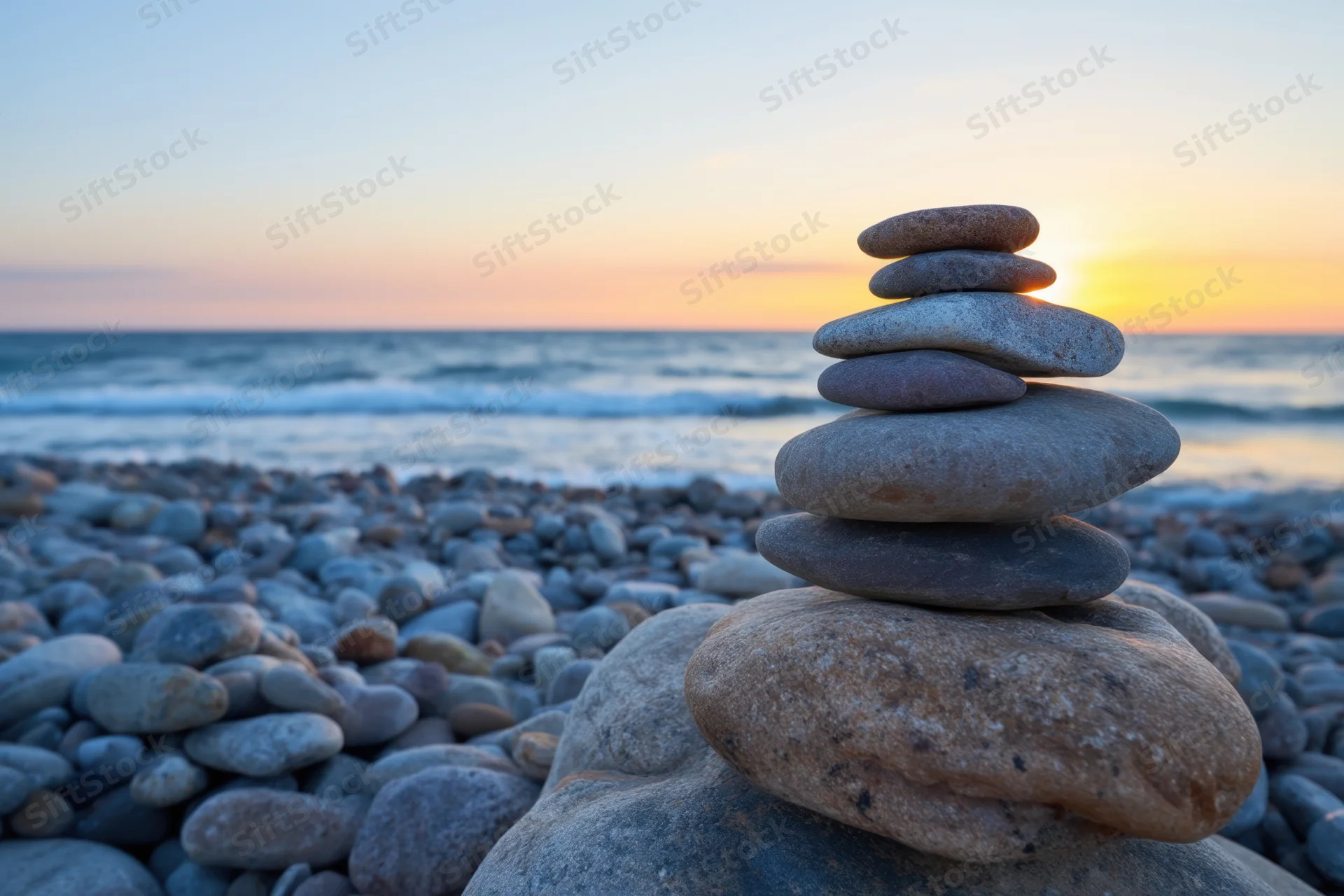 Stacked cairn of smooth stones on a pebble beach at sunset near the ocean