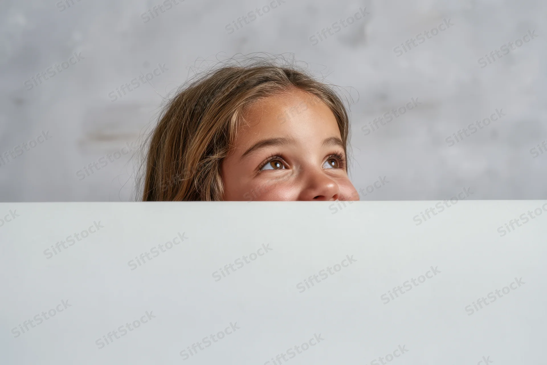 Young girl peeking over white surface with curious expression indoors