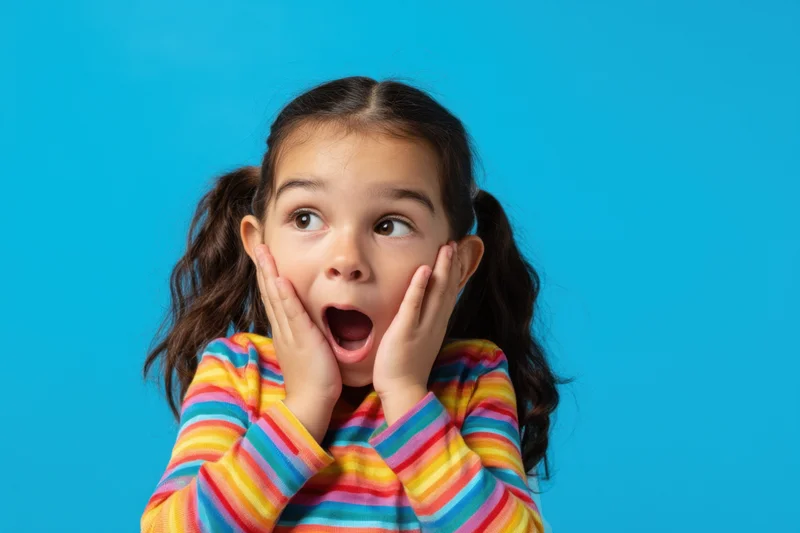 Young girl with pigtails in rainbow-striped shirt showing surprised expression against blue background