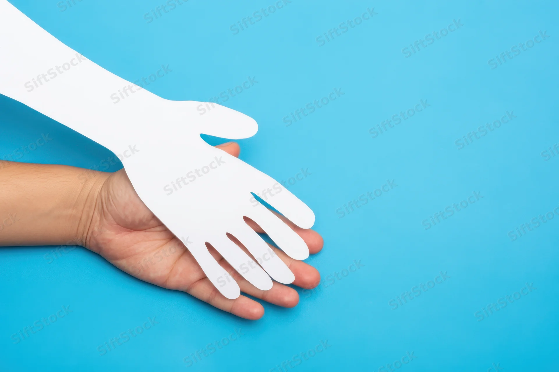 A human hand holding a white paper cutout of a hand against a blue background