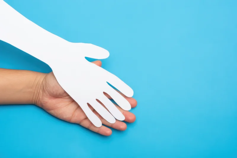 A human hand holding a white paper cutout of a hand against a blue background
