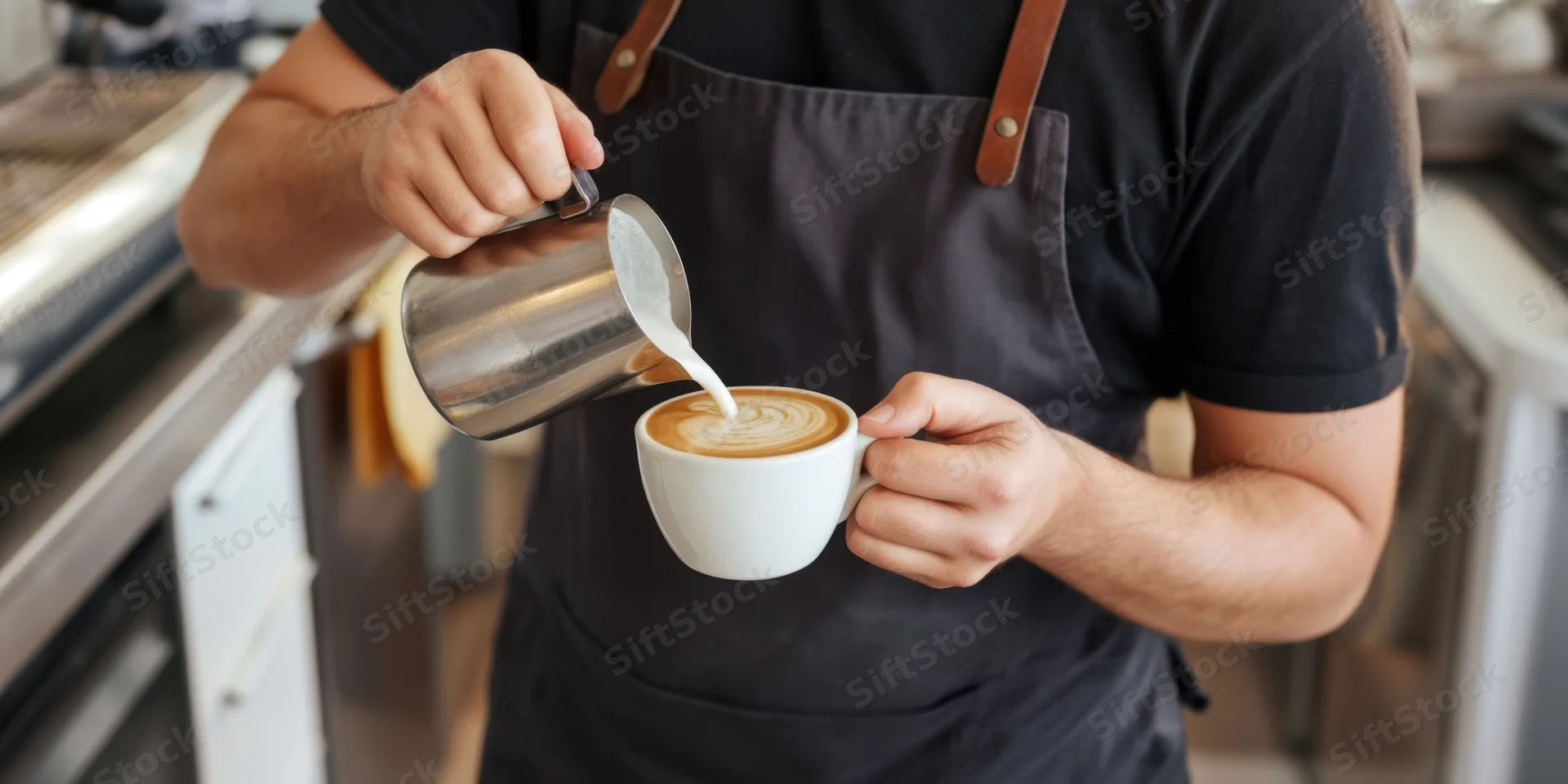 Barista pouring steamed milk into a latte cup in a café kitchen