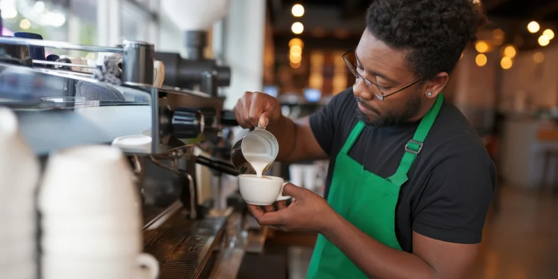 Barista pouring steamed milk into a white cup at a cafe counter