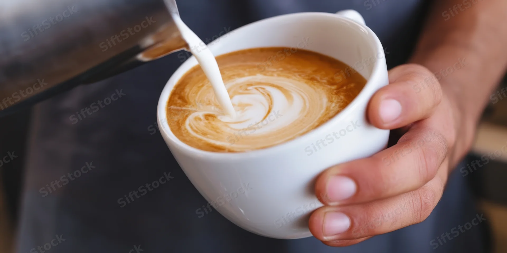 Barista pouring milk into a white cup to create latte art swirl