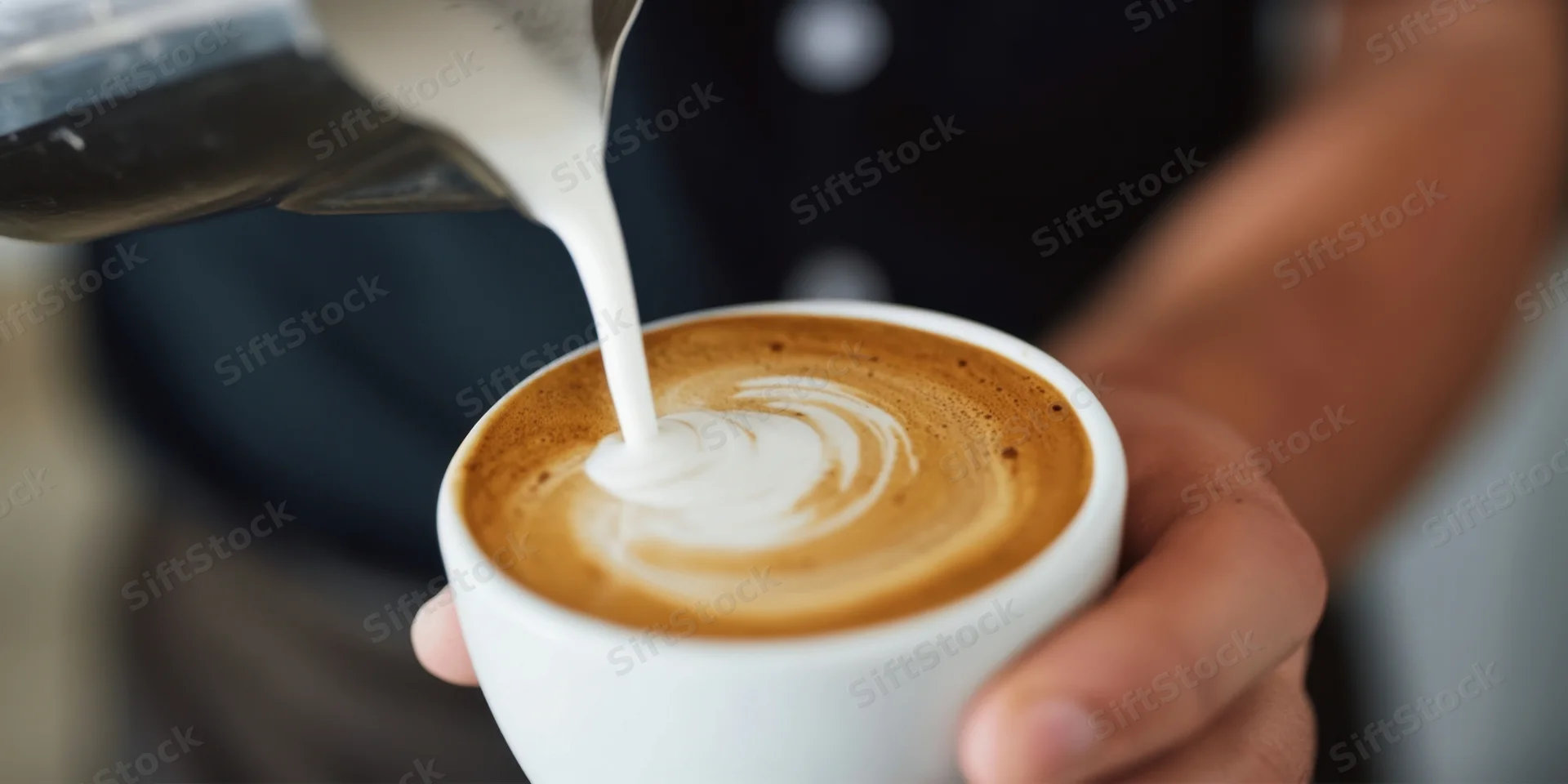 Barista pouring milk into a white cup to create latte art