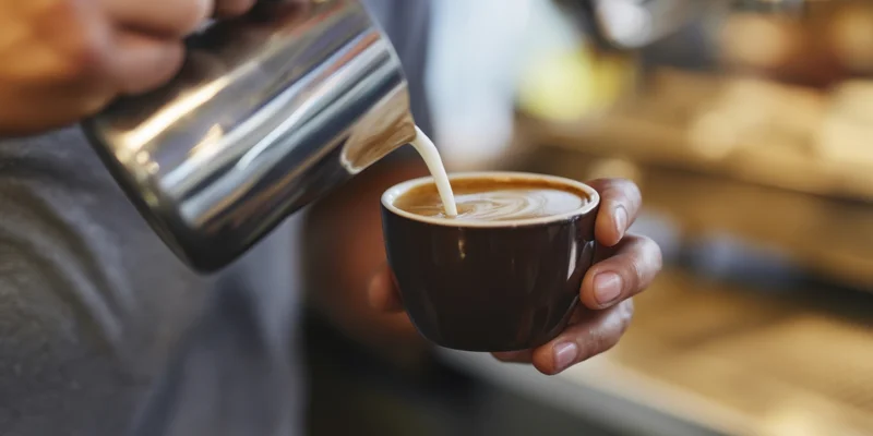 Barista pouring steamed milk into a ceramic cup to create latte art in a cafe
