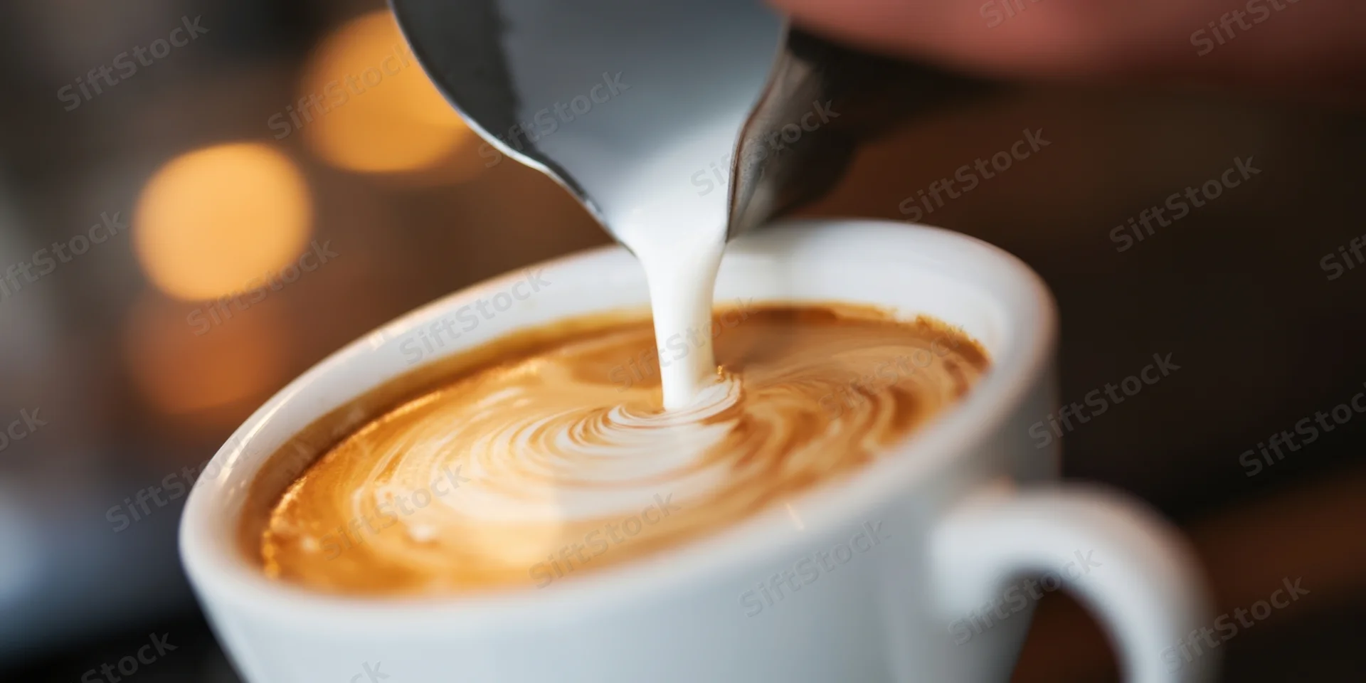 Barista pouring steamed milk into a latte cup to create foam swirls in a cafe