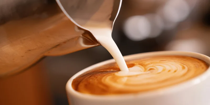Barista pouring steamed milk into a latte cup to create foam art