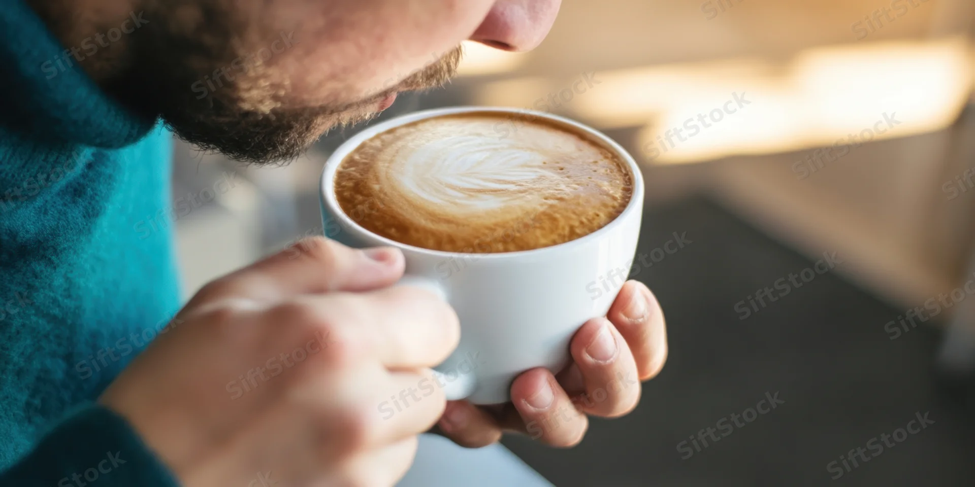 Man sipping coffee from a white ceramic cup indoors