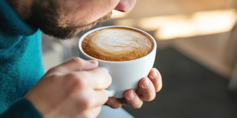 Man sipping coffee from a white ceramic cup indoors