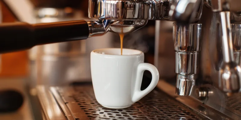 Espresso machine pouring coffee into a white cup on a metal drip tray
