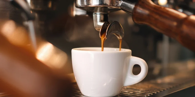 Espresso machine dispensing coffee into a white cup on a metal drip tray