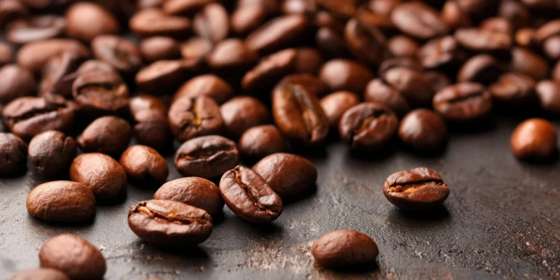 Roasted coffee beans scattered on a dark textured surface in closeup view