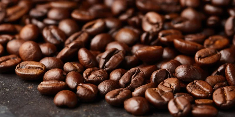 Close-up of glossy roasted coffee beans scattered on a dark surface